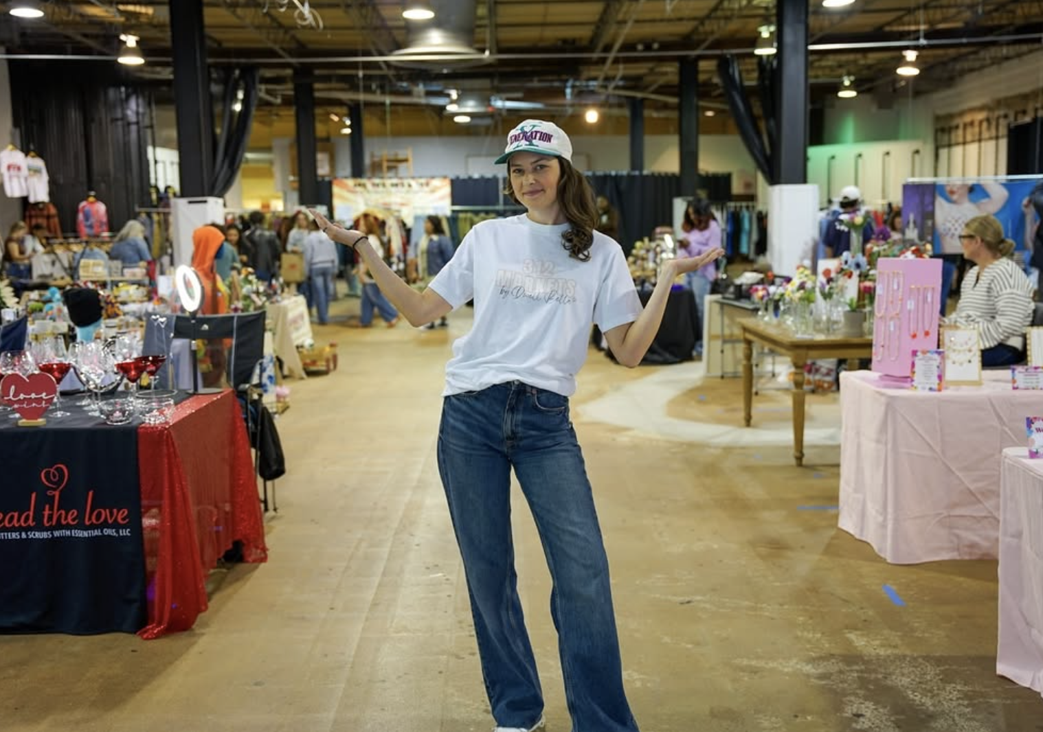 Event host positioned between vendor tables at a pop-up market, helping shoppers feel confident discovering small businesses in a lively event space